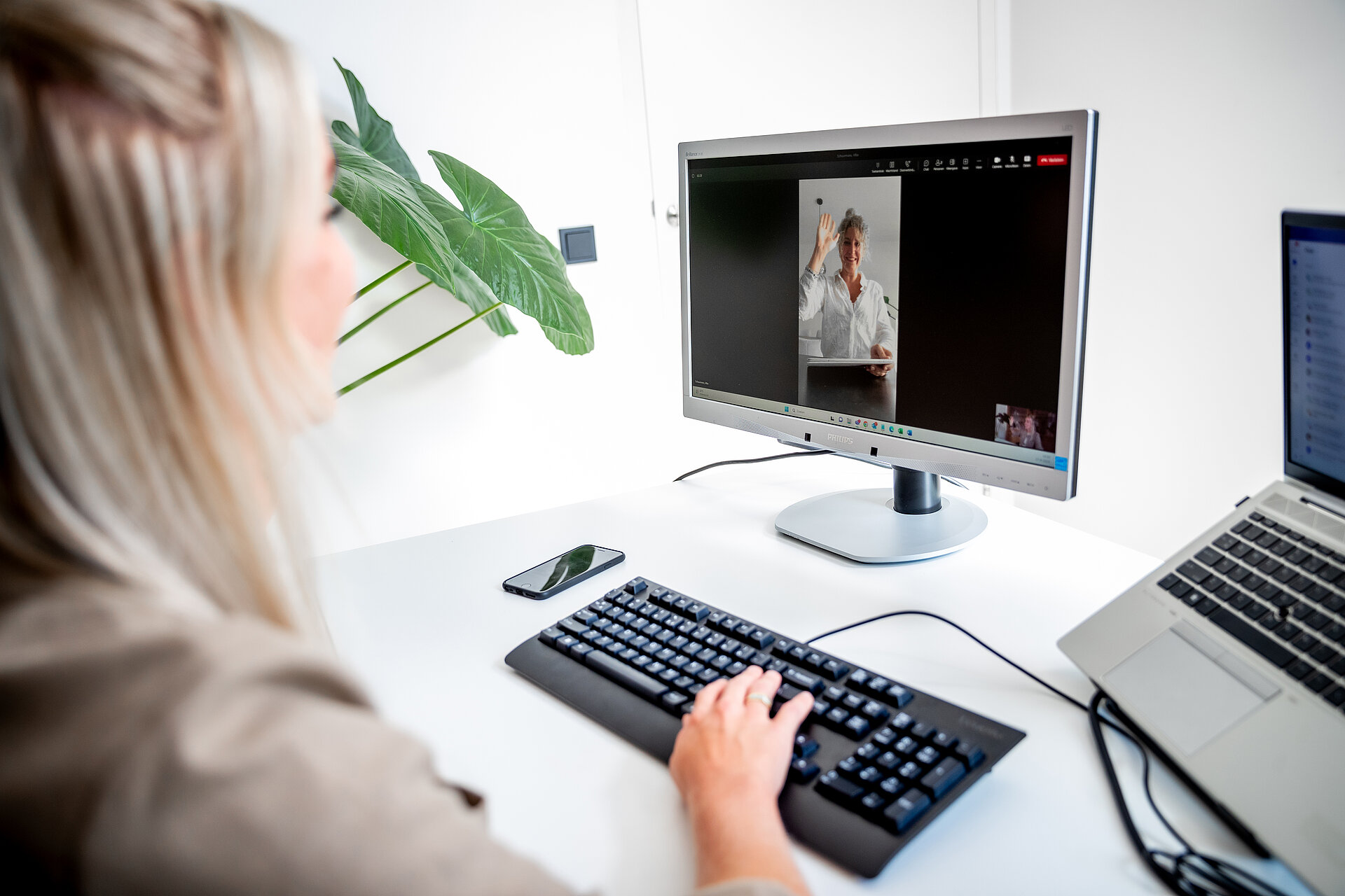 vrouw achter een beeldscherm met daarop een zwaaiende vrouw