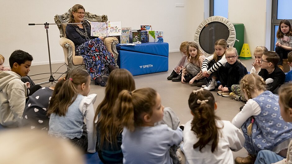 Burgemeester Fleur Gräper leest voor aan leerlingen van basisschool De Stappen die aan haar lippen gekluisterd zijn.