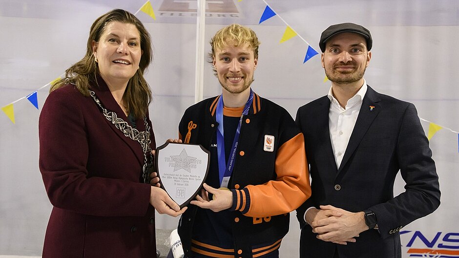 De burgemeester met wethouder Maarten van Asten en shorttracker Friso Emons met een bord in zijn handen in het midden