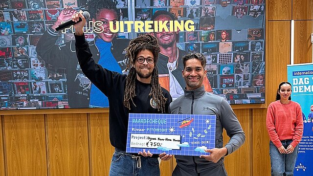 Twee jongens met een cheque in hun handen met daarop een geldbedrag