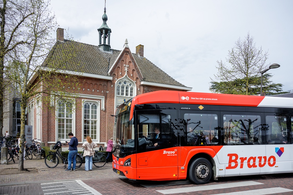De bus rijdt voorbij aan het oude raadhuis in Udenhout er staan wat mensen op de stoep die daarnaar kijken