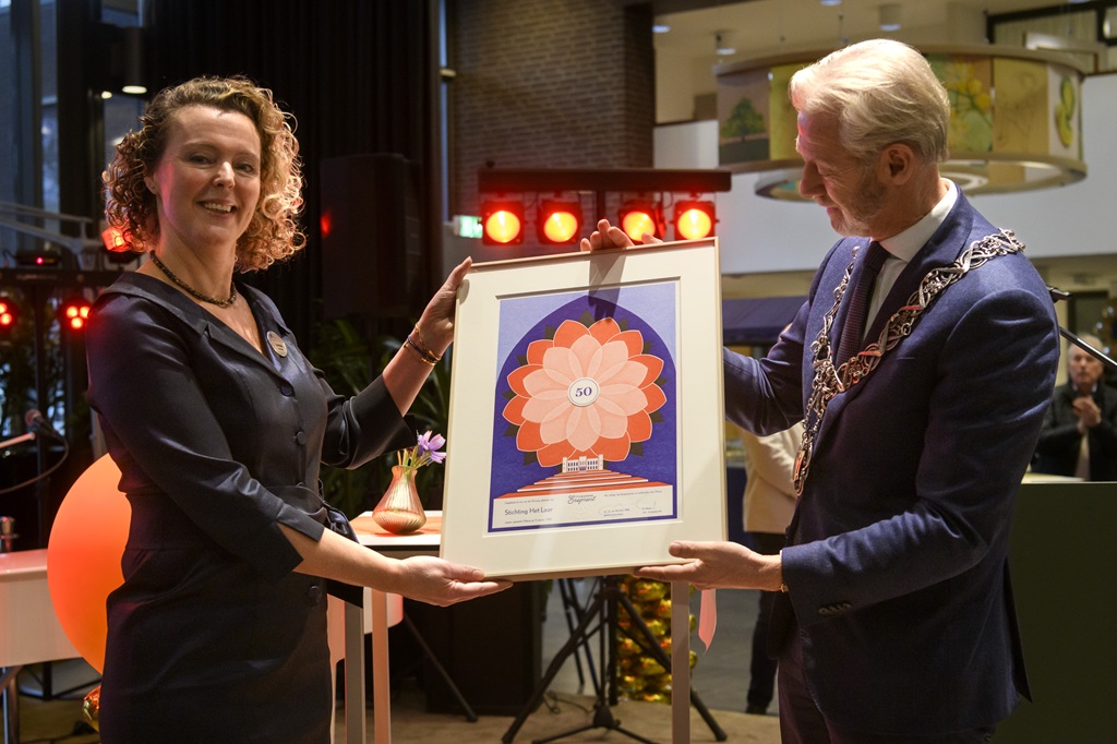 Een vertegenwoordiger van Het Laar en waarnemend burgemeester Onno Hoes samen met de Tilburgse Ereprent in hun handen die ze tonen aan de aanwezigen.