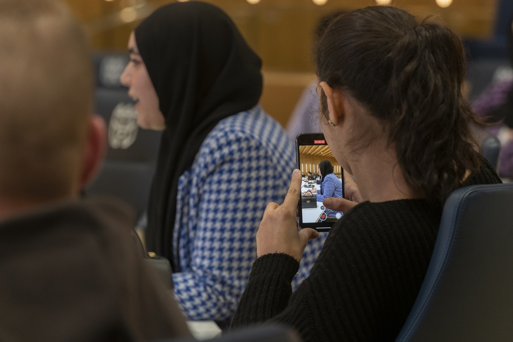Meisje met hoofddoek met andere jongeren in een ruimte terwijl ze praat en gefilmd wordt