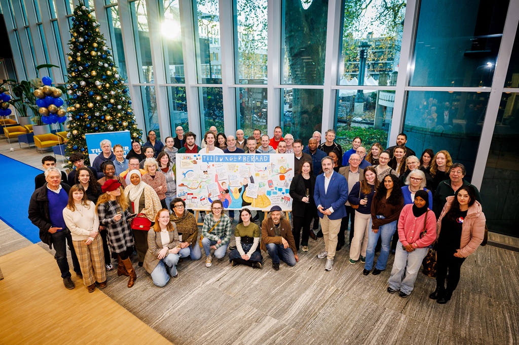Groep inwoners die hebben deelgenomen aan het Tilburgerberaad met een grote tekening met daarop Tilburgerberaad in hun handen.