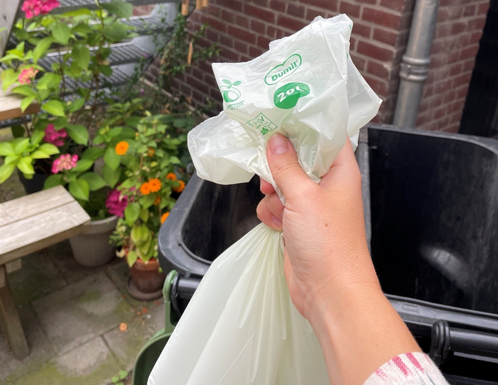 Een hand houdt een afbreekbare gft zak vast bij de kliko