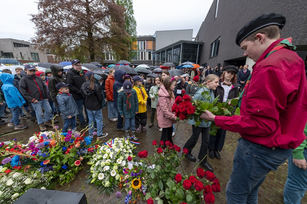 Een eerdere herdenking in het Vrijheidspark in Tilburg met veel bloemstukken op de foto en een jongen van de scouting die ze neerlegt.