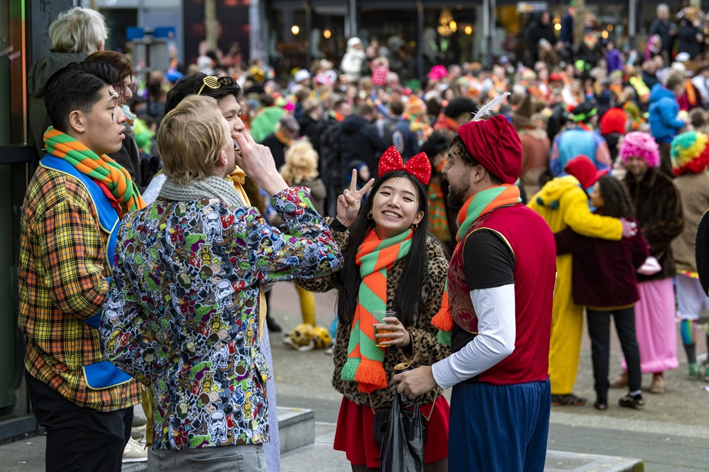Vier carnavalsvierders babbelen gezellig met elkaar tijdens carnaval. Ze hebben o.a. de mooie groen-oranje sjaal om.