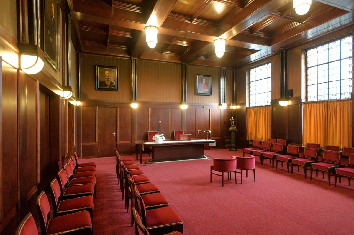 Willem II zaal in het Paleisraadhuis met rode vloerbedekking, rode fluwelen stoeltjes en donker houten wandbekleding